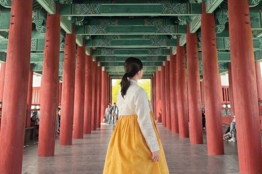 A corridor with red pillars and a person in traditional attire walking away. 2
