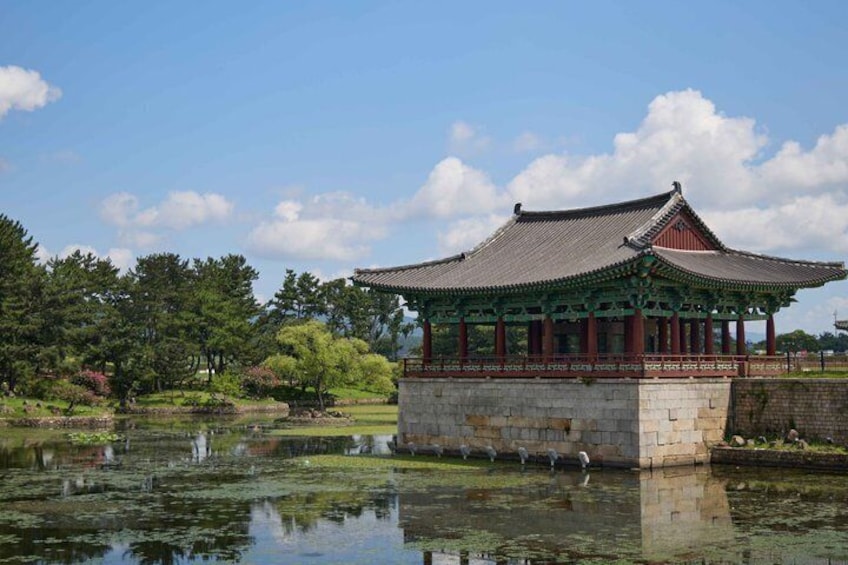 A traditional Korean pavilion by a calm pond with trees and a clear sky. 4