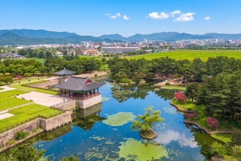 A traditional pavilion by a calm lake, surrounded by lush greenery and distant mountains. 5