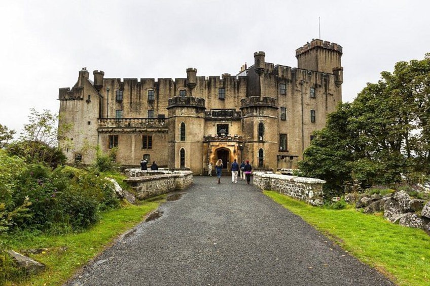 A historic castle with a central entrance, surrounded by a gravel pathway and lush greenery. 3
