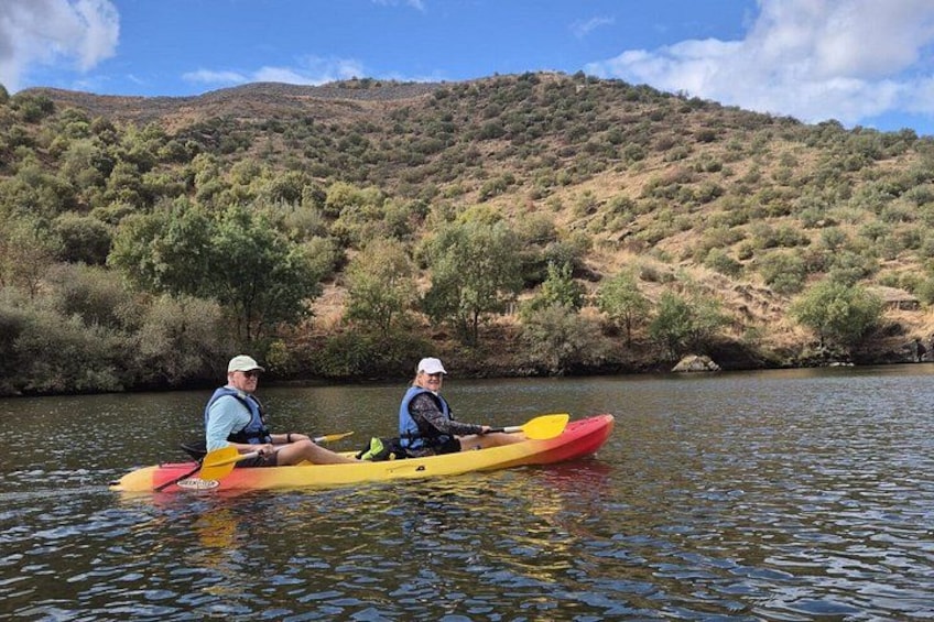 Two people kayaking on a river with a hilly landscape in the background. 5
