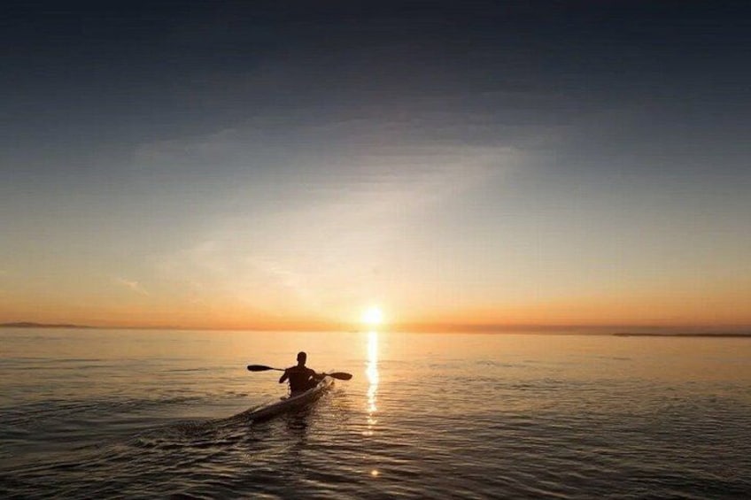 A person kayaking on calm water during sunset. 1