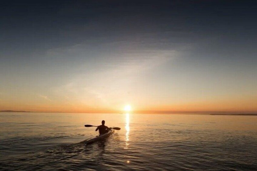 A person kayaking on calm water during sunset. 1