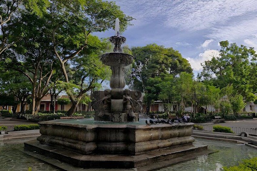 A fountain with a statue, surrounded by trees and buildings. 3