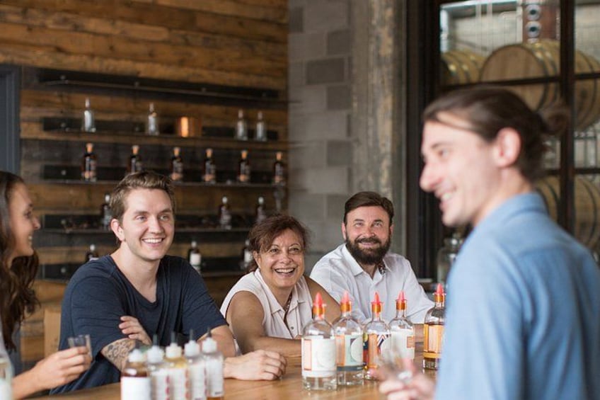 A group of people sitting at a table with bottles and glasses, in a room with wooden shelves and barrels in the background. 2