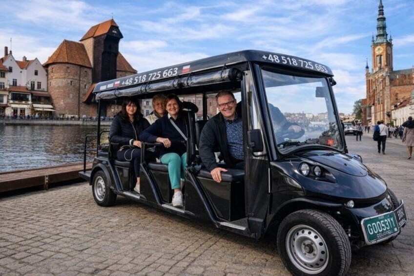 A black electric vehicle with passengers, parked by a historic building with a clock tower. 3