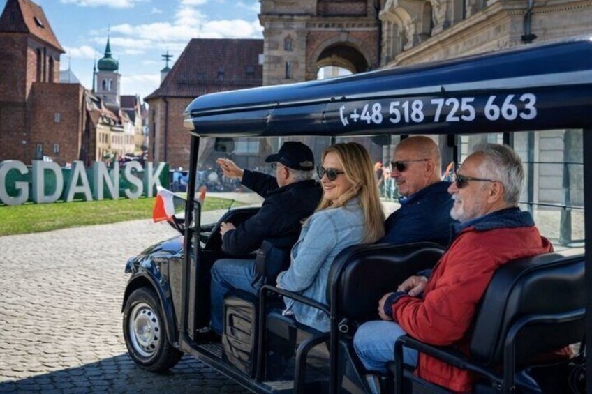 A vintage car with a contact number, passengers, and a historic building in the background. 1