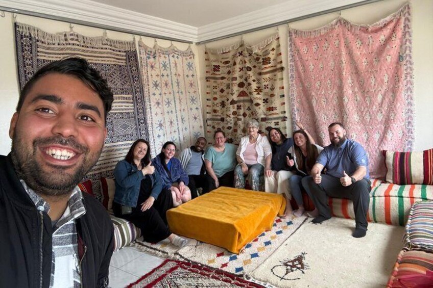 A group of people sitting on a couch and a bed in a room with patterned curtains and rugs. 1