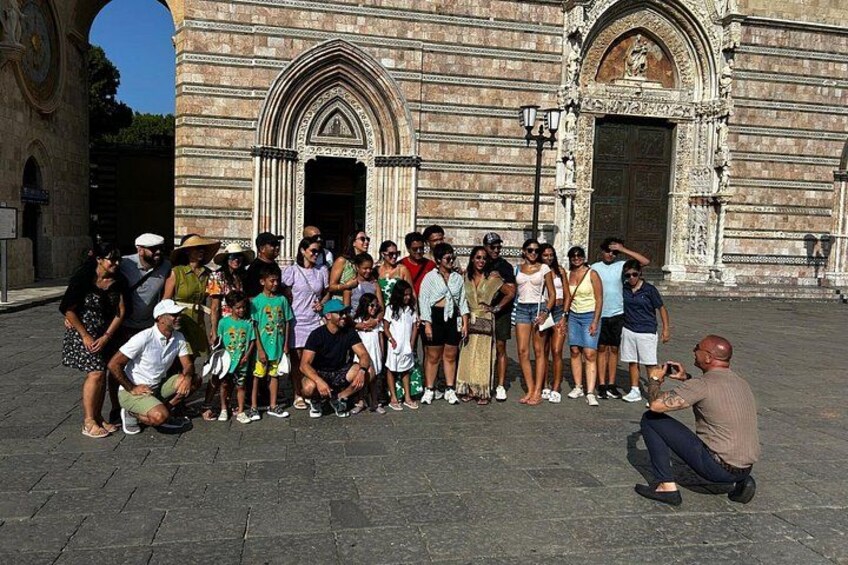 A group of people posing in front of a historic building with arched doorways and detailed stonework. 3