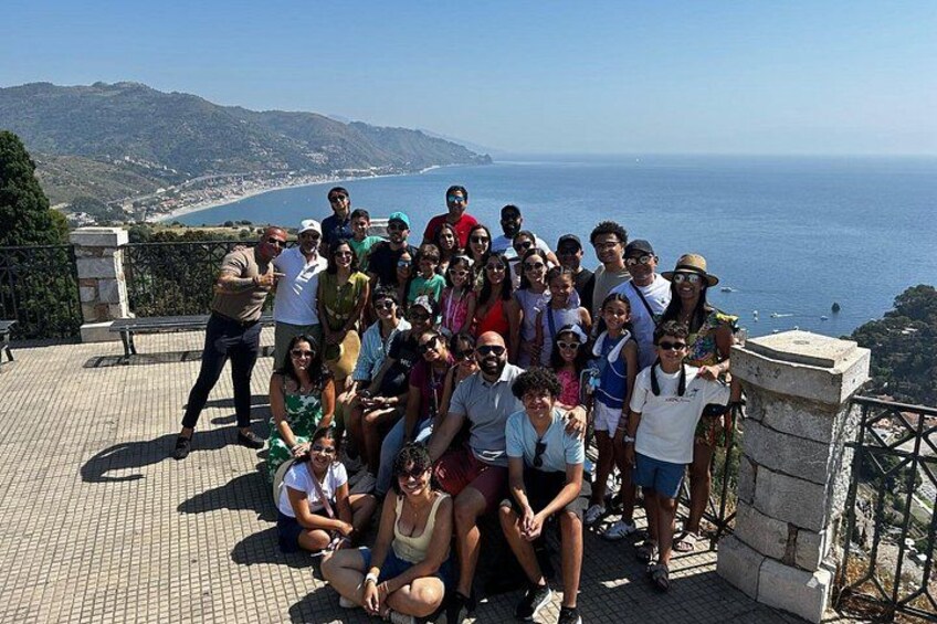 A group of people on a terrace overlooking a coastal landscape with hills and the sea. 5