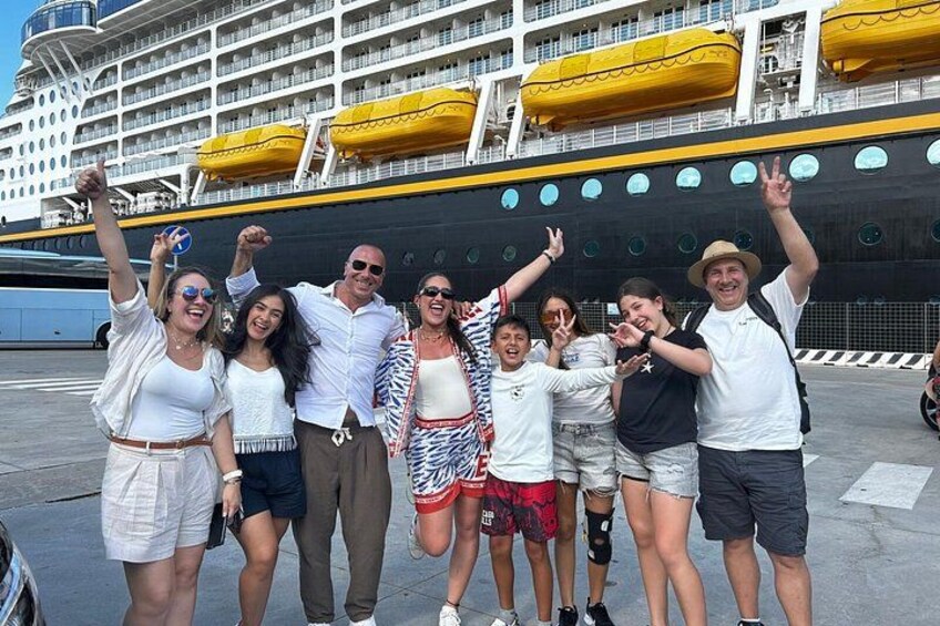 A group of people posing in front of a large cruise ship with multiple decks and lifeboats. 4