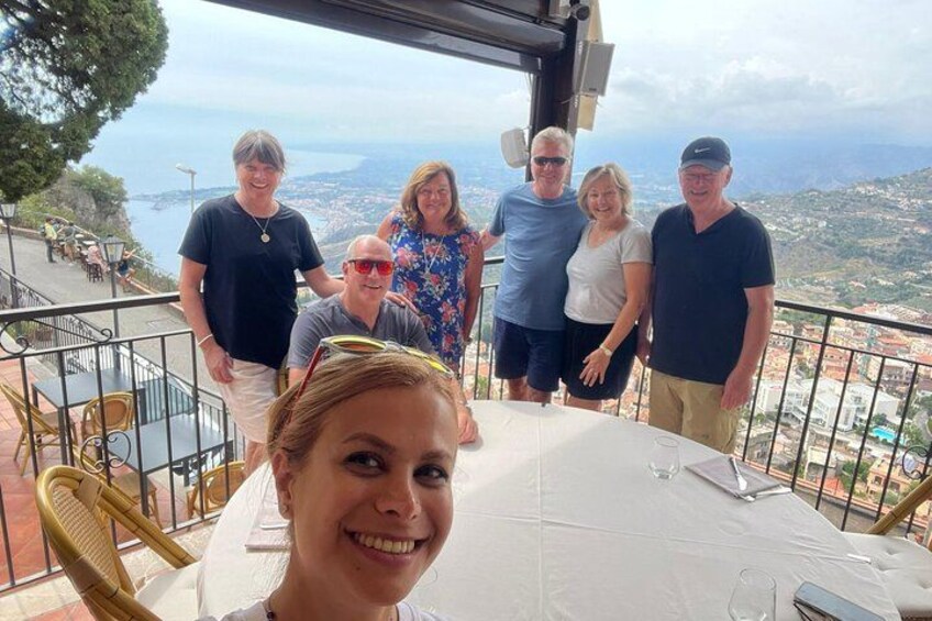 A group of people standing at a table with a scenic view of a coastal landscape in the background. 2