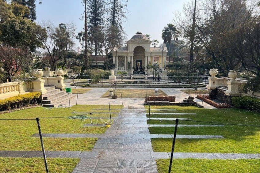 A formal garden with a central fountain, symmetrical pathways, and classical architecture. 3