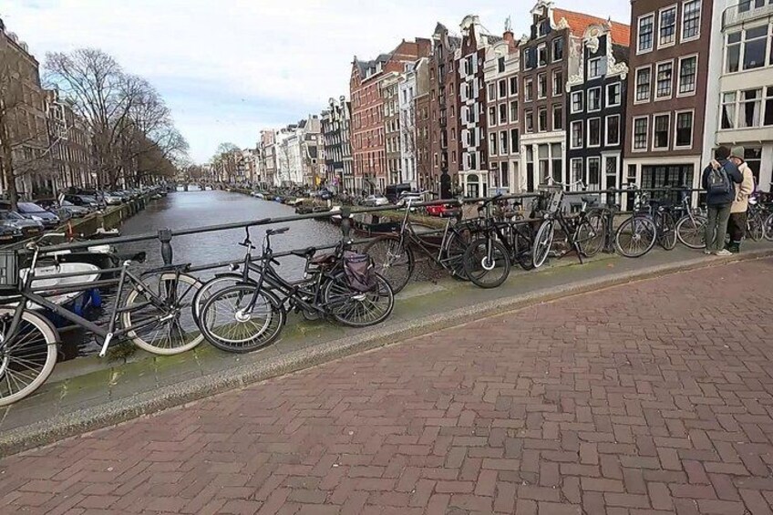 A canal with bicycles parked along the side, a row of historic buildings, and a paved walkway. 3
