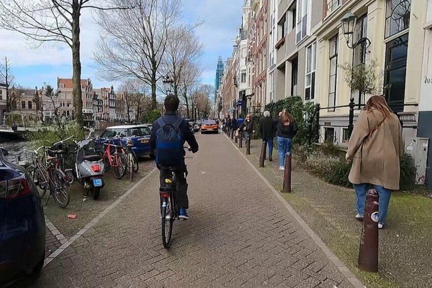 A cyclist riding on a brick pathway, parked bicycles, and buildings along a canal. 4