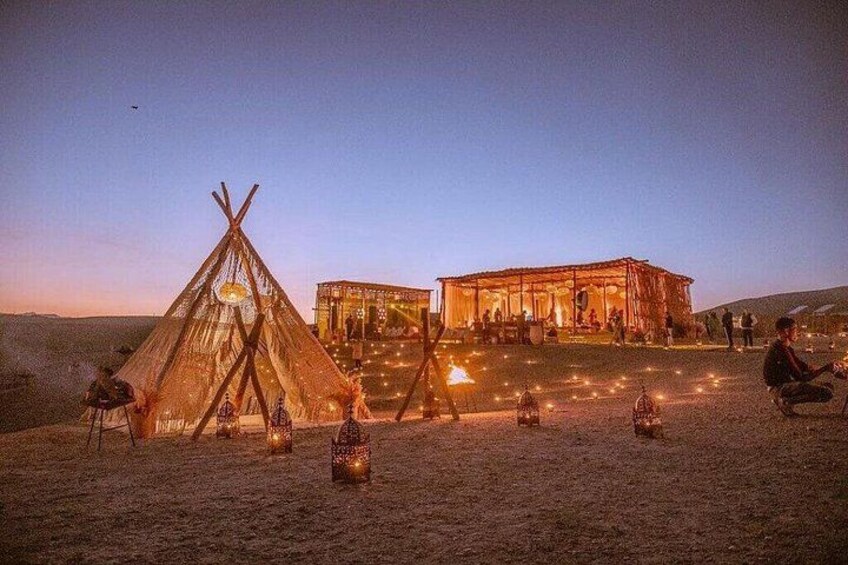A desert campsite with a teepee and a wooden structure at dusk. 5