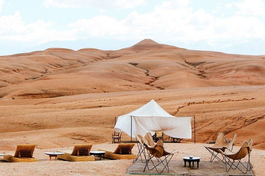 A desert campsite with tents, lounge chairs, and a mountainous backdrop. 2