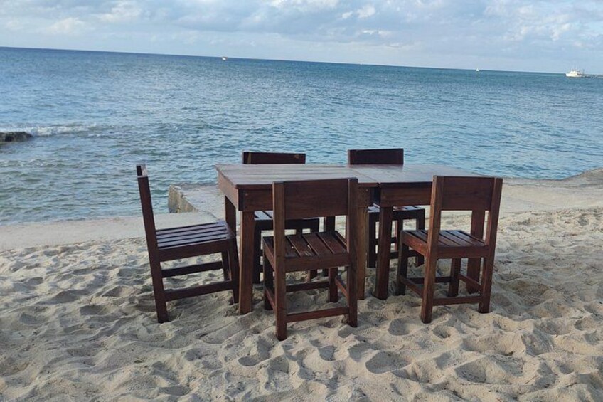 A wooden table and chairs on a sandy beach with the ocean in the background. 3