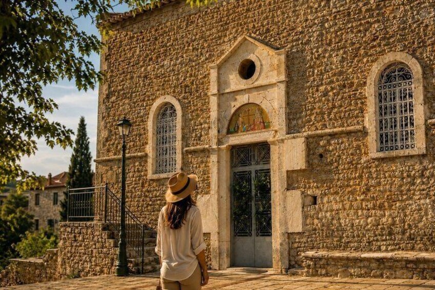 A stone building with arched windows and a door, a person standing in front, and a street lamp. 1