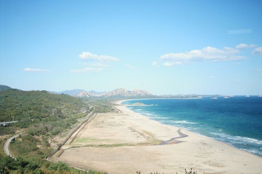 A coastal landscape with a beach, a road, and distant mountains. 1