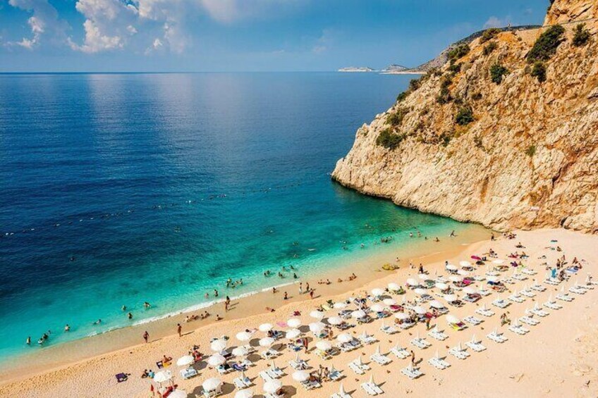 A beach with clear turquoise water, a sandy shore, and a rocky cliff. 3