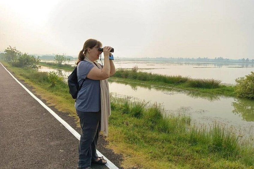 A person taking a photograph with a camera, standing on a road beside a body of water. 3