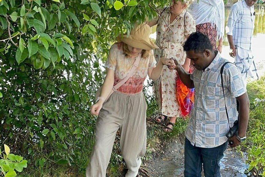 A person in a straw hat and light-colored clothing standing in a natural setting with greenery and a water body. 4