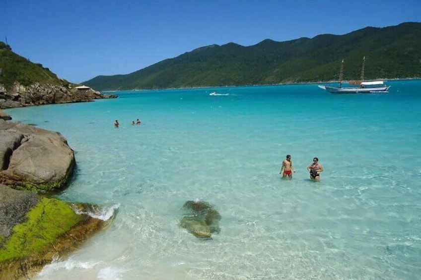A clear turquoise sea with people swimming, a boat, and rocky shores with greenery. 5
