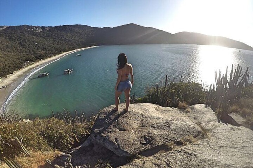 A person standing on a rock overlooking a coastal area with boats on the water and a beach in the distance. 3