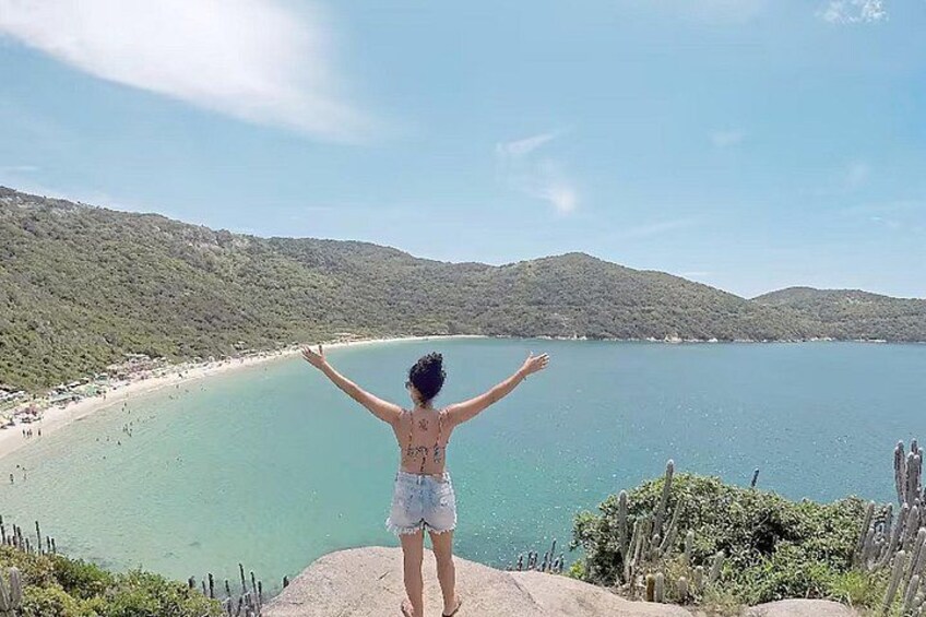 A person standing on a cliff with arms outstretched, overlooking a beach and a body of water. 2