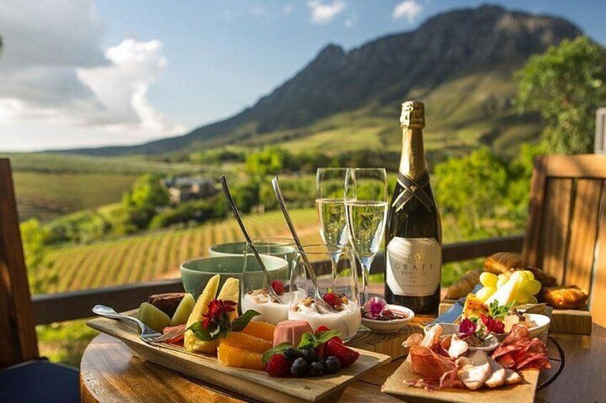 A table with food and drinks, a bottle of wine, and a scenic vineyard view. 5