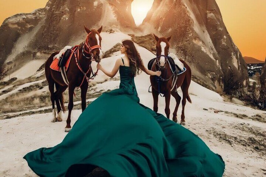 A person in a green dress with two horses in a snowy landscape with mountains in the background. 3