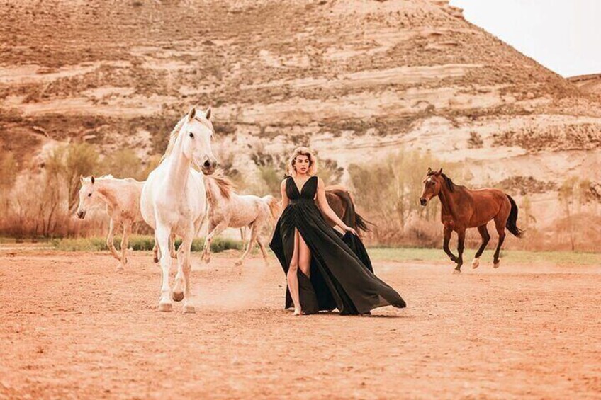 A person in a flowing black dress with horses in the background. 2