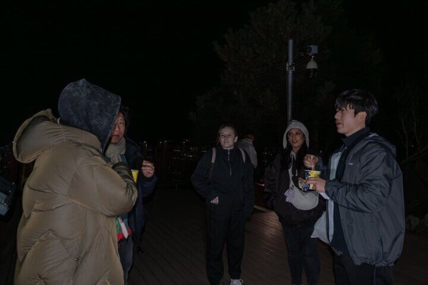 A group of people standing on a sidewalk at night. 4