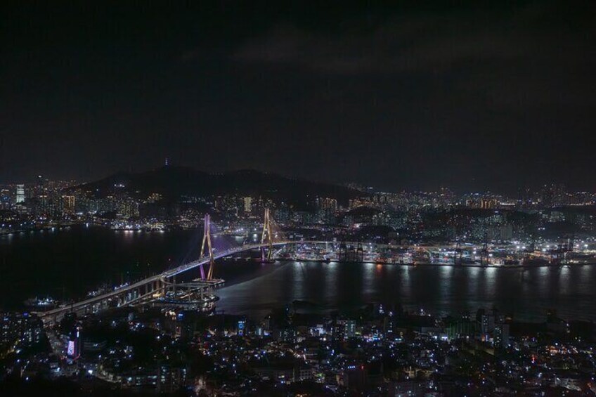 A nighttime cityscape with a prominent bridge and a body of water. 1