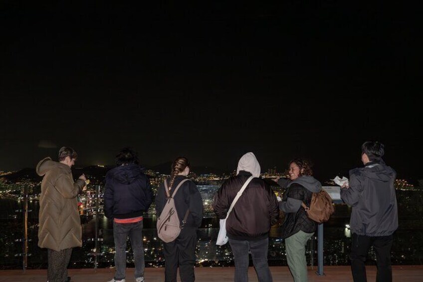 A group of people standing on a balcony overlooking a cityscape at night. 3