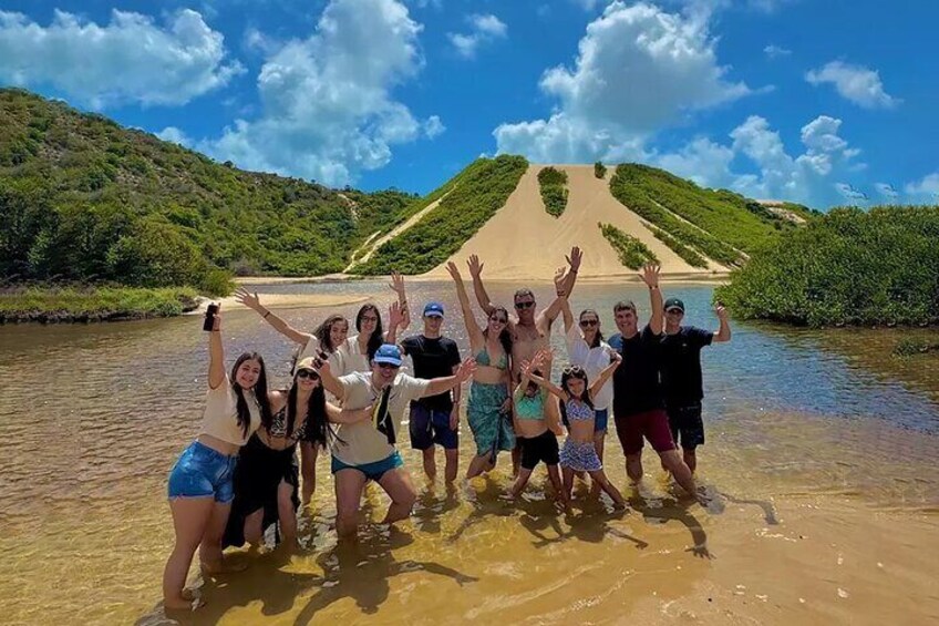 A group of people posing in front of a sandy hill with a river. 1
