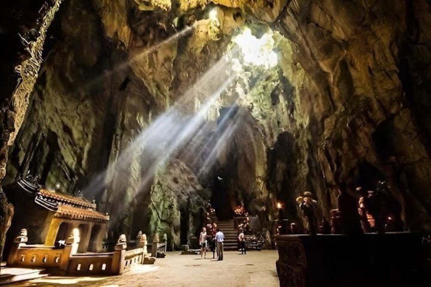 A cave with stalactites, a small shrine, and people exploring. 2