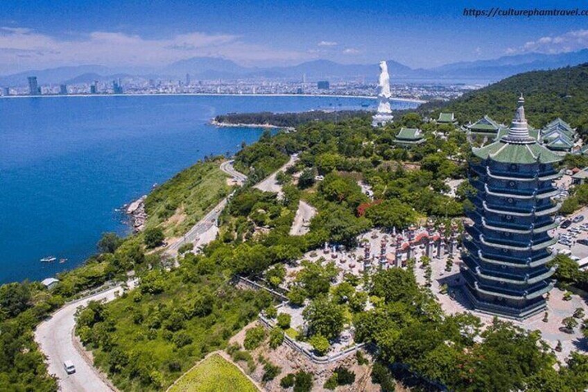 A coastal cityscape with a pagoda, a large statue, and a body of water. 1