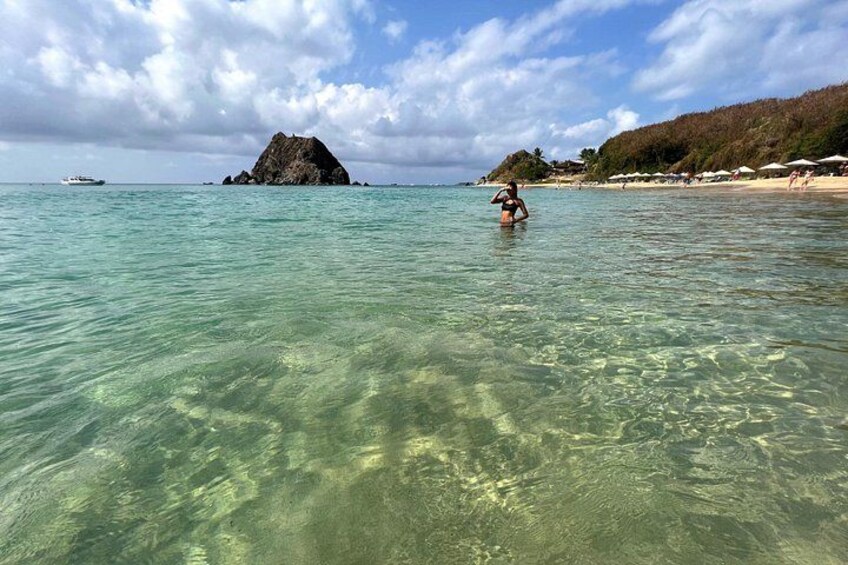 Clear turquoise water, a rocky island, and a beach with umbrellas. 4