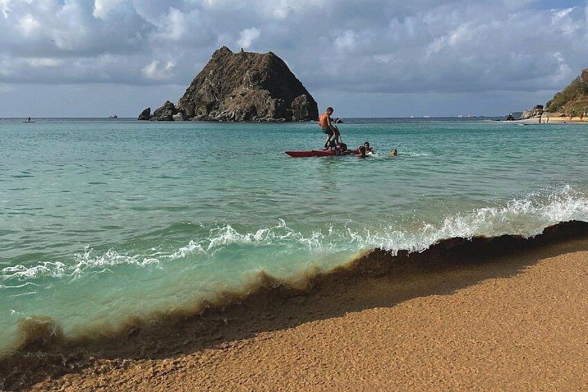 A beach with clear turquoise water, a rocky outcrop, and a person on a red paddleboard. 5
