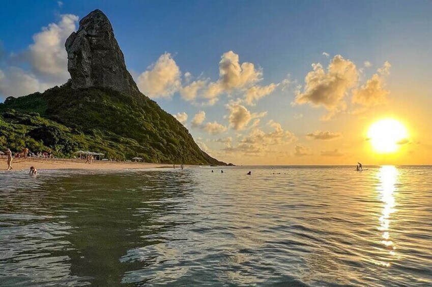 A coastal landscape with a prominent rock formation, calm sea, and a sunset. 3