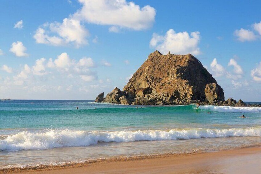 A beach with clear turquoise water, a large rocky island, and gentle waves. 2