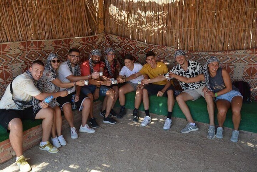 A group of people sitting on a bench in a shaded area with a patterned wall behind them. 4