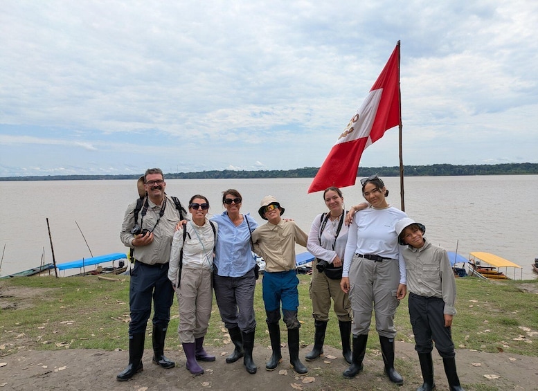 A group of people standing by a lake with a flag, boats, and a grassy area. 5