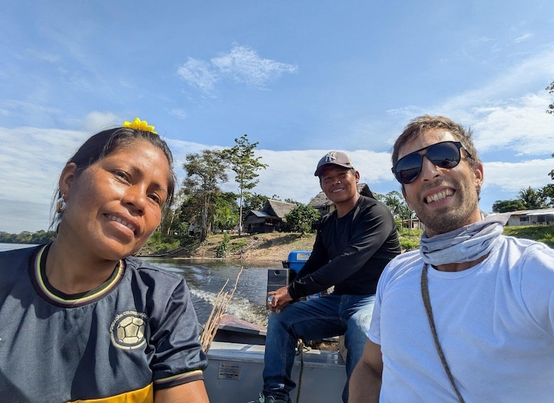 Three people on a boat with a river and houses in the background. 4