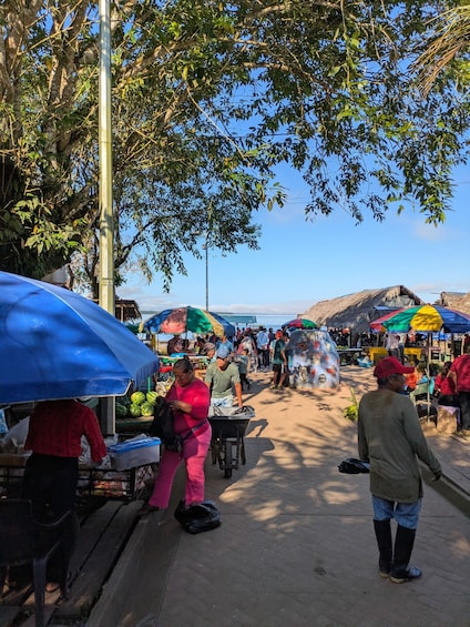 A bustling outdoor market with people shopping and vendors selling goods under colorful umbrellas. 2