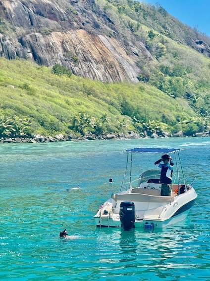 A boat with a person standing at the bow, another person swimming, and a rocky hillside in the background. 4