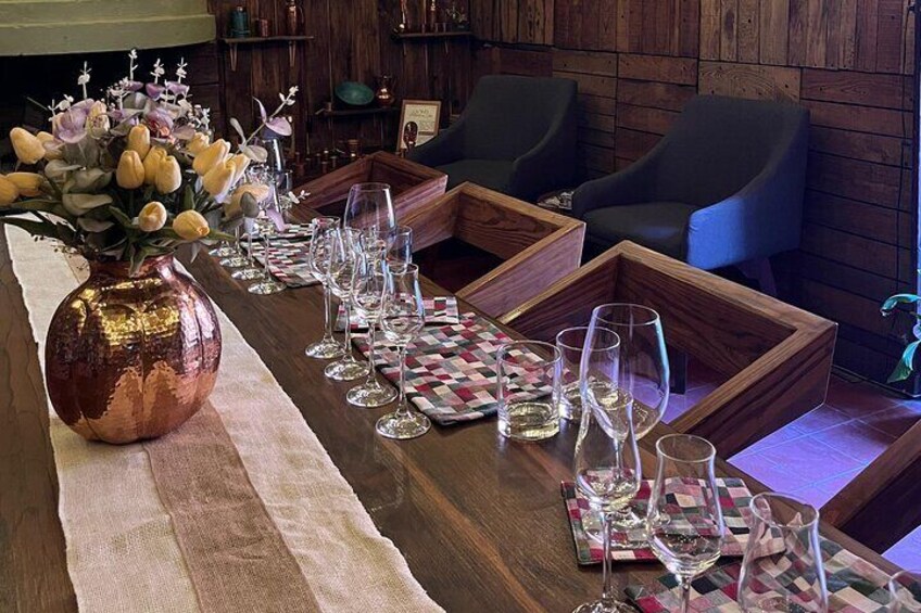 A wooden dining table set with wine glasses and a copper vase with flowers. 1