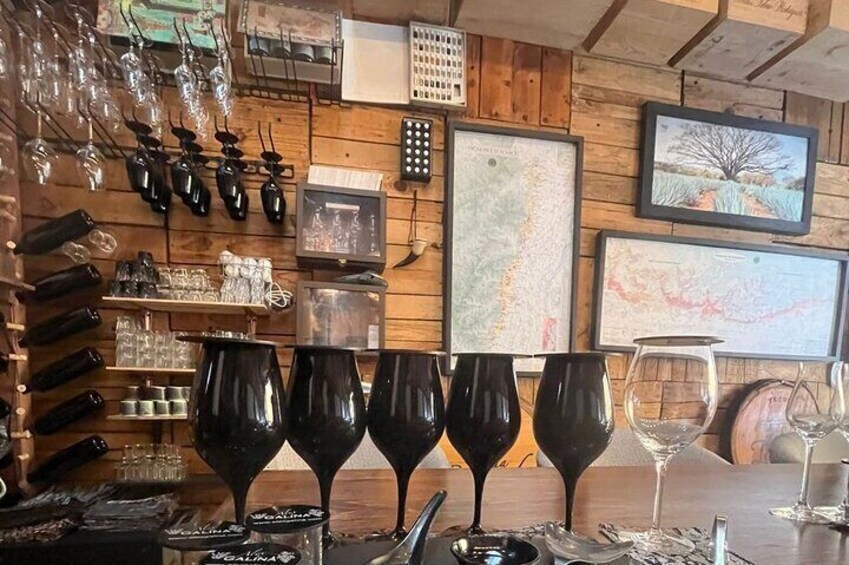 A bar with wine glasses and bottles, wooden walls, and framed maps. 2